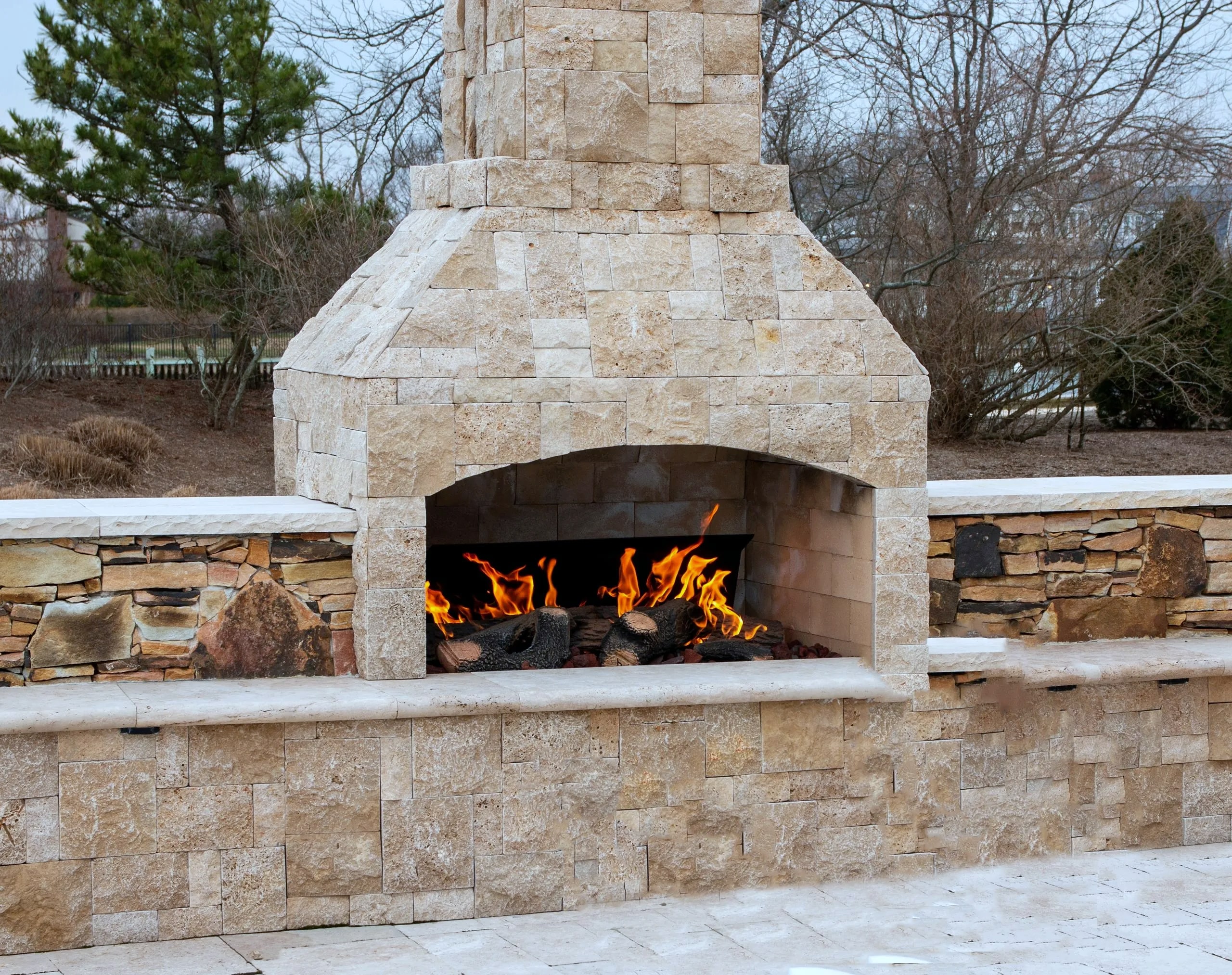 Stone outdoor fireplace with burning logs and stone seating walls